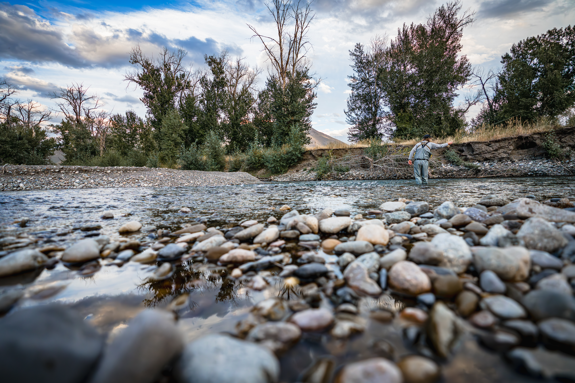 Angler on the river with rocks in the foreground. Photo by James Conrad