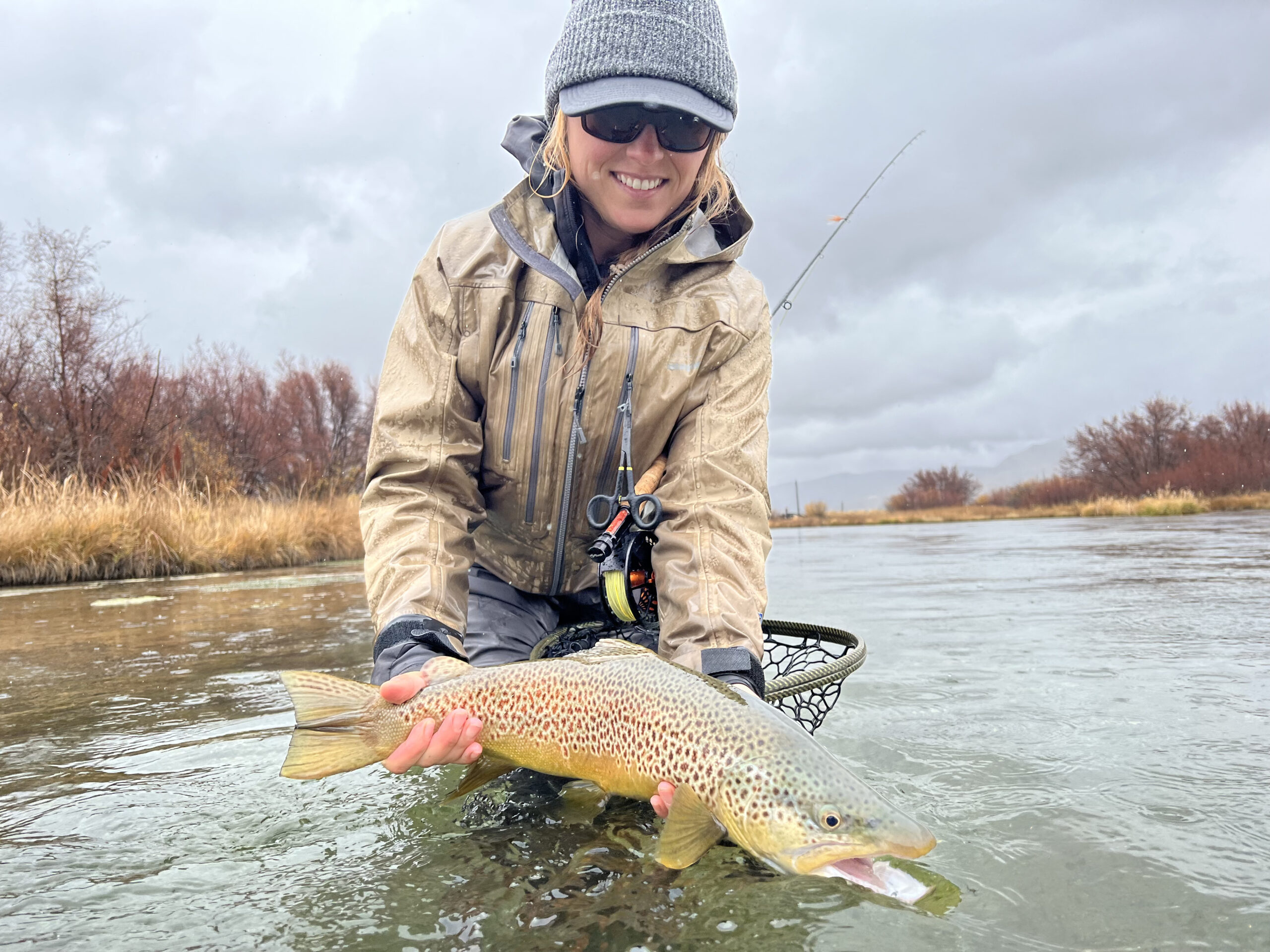 Female Angler holding up fish in the water with fall colors around