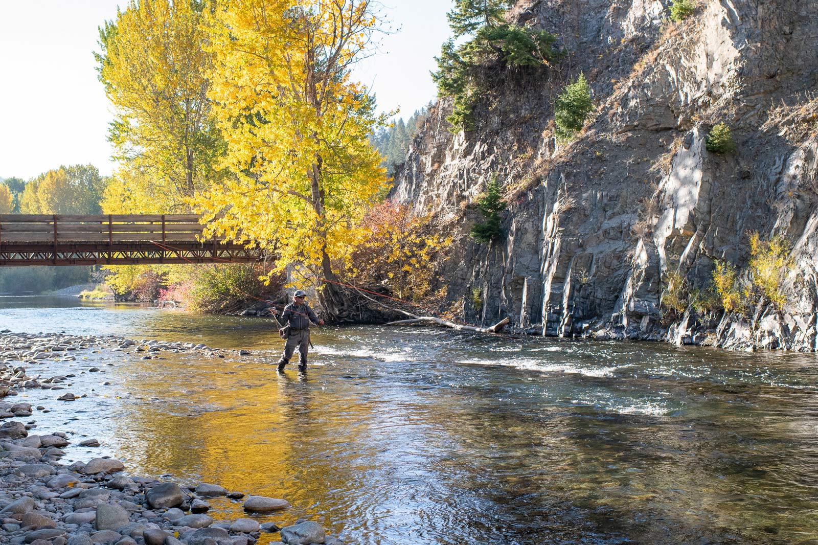 Angler fishing in the fall in the middle of the river with a bridge in the background