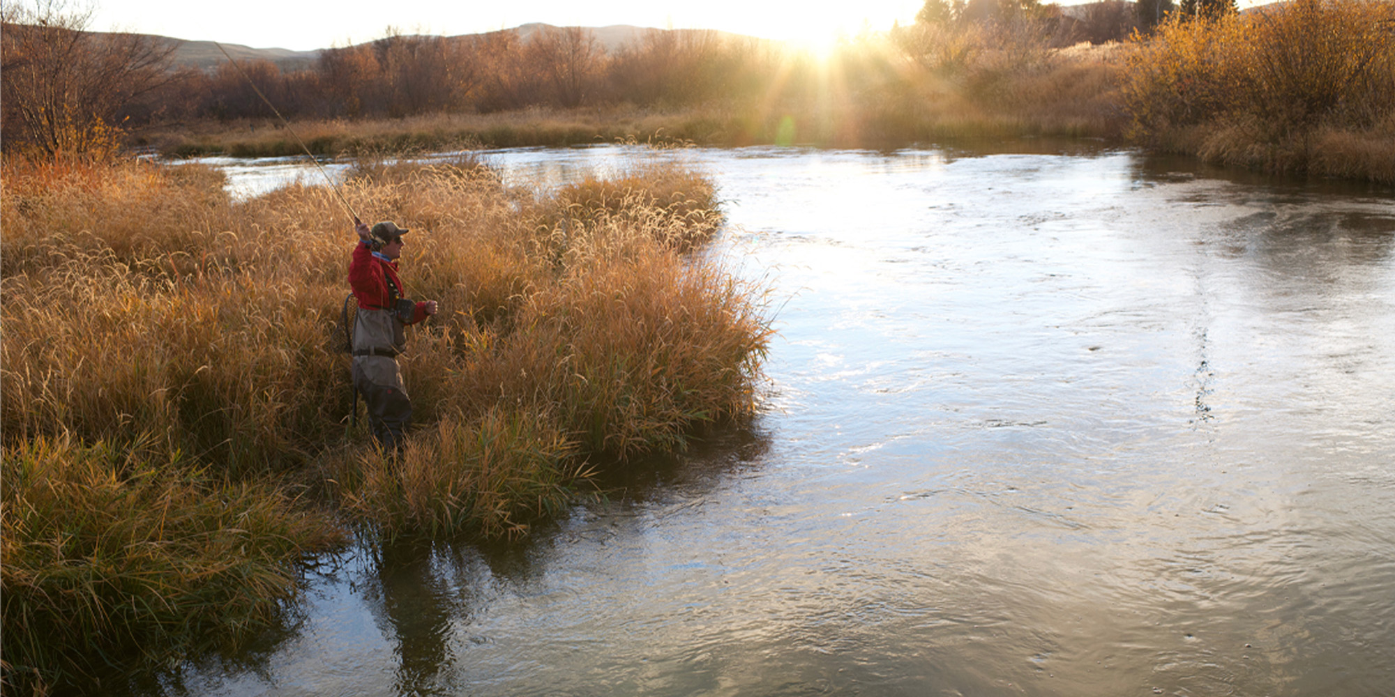 A person in waders fly-fishing in a river at sunrise during the fall fly fishing season in Idaho. Silver Creek Outfitters Sun Valley