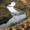 A person fly fishing in a winding river canyon during a Sun Valley winter, surrounded by brush and rocky hillsides.